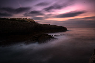 Rock formation in sea against sky during sunset