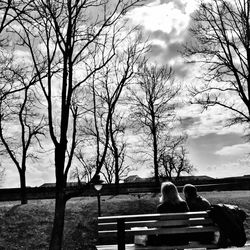 People sitting on bench against cloudy sky