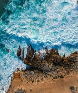 Aerial top view of sea waves hitting rocks on the beach with turquoise