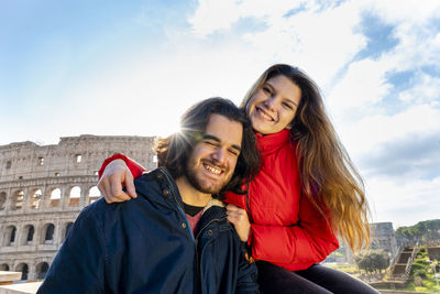 Young couple traveling to rome. the couple smiles and takes a selfie in front of the colosseum.