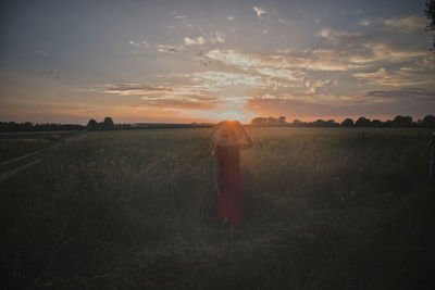 Woman standing on field against sky during sunset