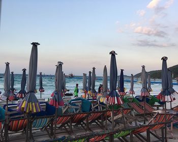 Chairs on beach by sea against sky during sunset