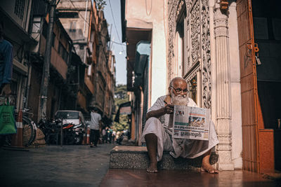 Man sitting on street amidst buildings in city