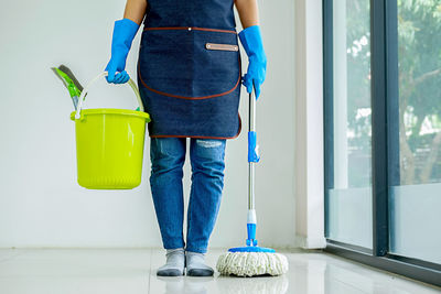 Low section of man holding bucket and mop while standing on floor