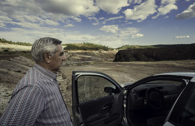 Side view of man standing by car on field