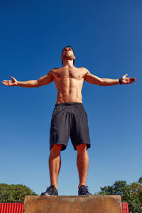 Low angle view of woman jumping against clear blue sky