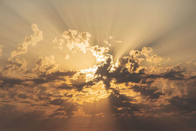 Low angle view of sunlight streaming through clouds during sunset