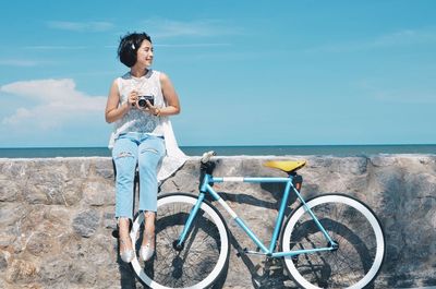 Young woman with bicycle standing at beach against sky