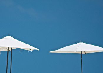 Low angle view of white parasols against clear blue sky
