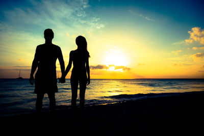 Silhouette friends on beach against sky during sunset