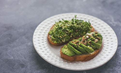 Vegan avocado sandwich with microgreens on a white plate on a gray background