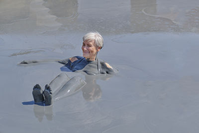 Senior woman relaxing in natural mud pool for wellness therapy.