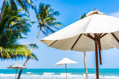 Lounge chairs on beach umbrella by sea against sky