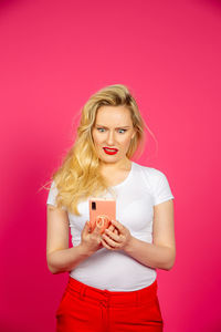 Young woman using mobile phone against pink background