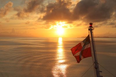 Flag over sea against sky during sunset