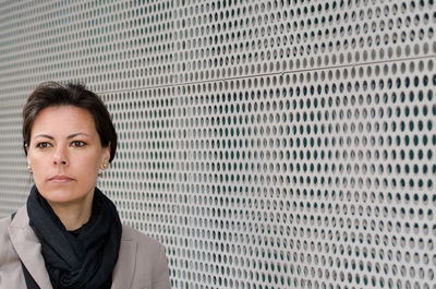 Mature woman looking away while standing by metal grate