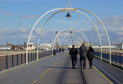 Rear view of people walking along pier against sky