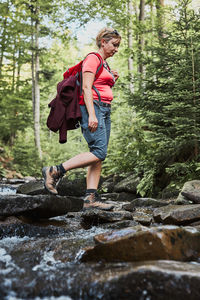 Woman with backpack hiking in mountains, spending summer vacation. woman crossing mountain stream