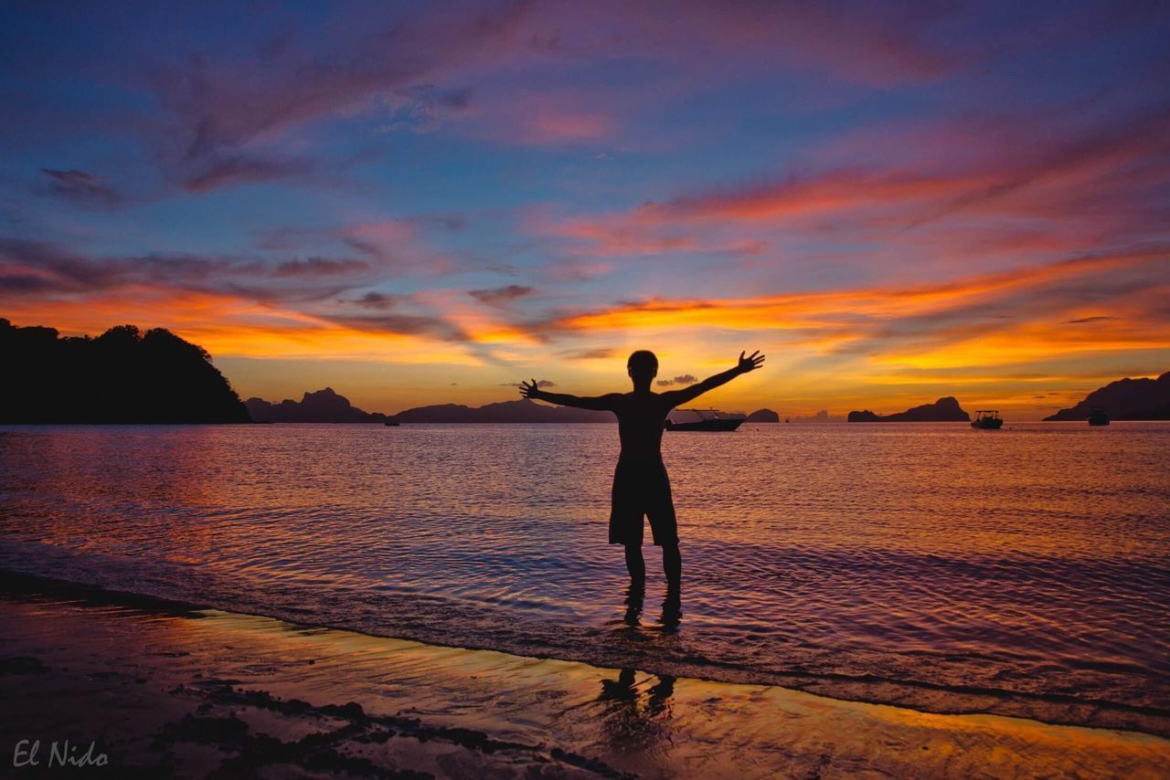 SILHOUETTE BOY STANDING ON BEACH AGAINST SKY DURING SUNSET