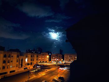 Illuminated street amidst buildings against sky at night