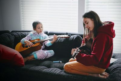 Two little girls playing guitar sitting on sofa at home