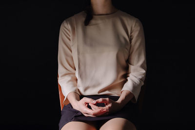 Midsection of woman sitting on chair against black background