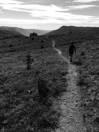 Rear view of man walking on field against sky