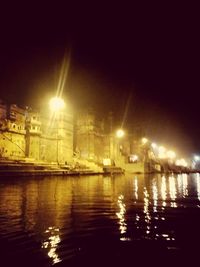 Illuminated city by river against sky at night