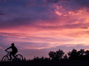 Silhouette man riding bicycle against sky during sunset