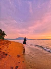 Woman walking at beach against sky during sunset