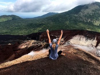 Rear view of woman with arms raised sitting on mountain