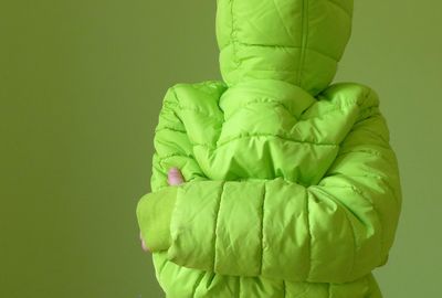 Close-up of person in jacket with face covered against green background