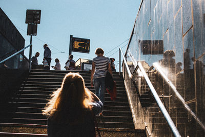 Rear view of people climbing on staircases in city during sunny day