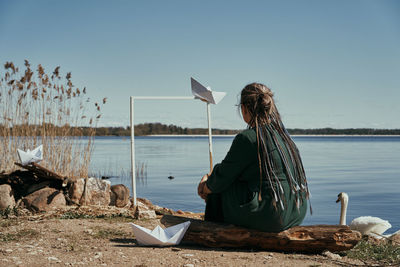 Woman sitting on shore by lake against sky