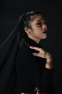 Young woman looking away while standing against black background