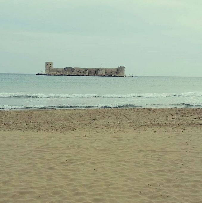 sea, beach, sand, horizon over water, shore, water, sky, built structure, architecture, tranquil scene, tranquility, wave, building exterior, scenics, nature, coastline, beauty in nature, day, incidental people, outdoors