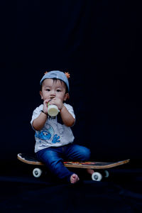 Full length of cute baby boy sitting against black background