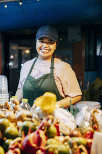 Portrait of smiling female juice vendor standing at stall in food market