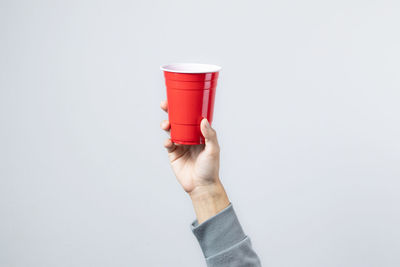 Close-up of hand holding red cup over white background