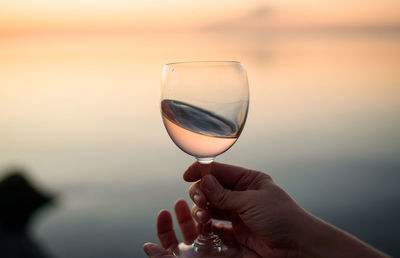 Midsection of person holding wineglass against sunset