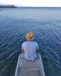 Rear view of man sitting on pier over sea