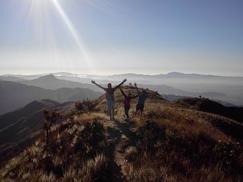 Friends with arms raised standing on mountain against sky