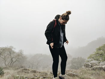 Young woman standing on field in foggy weather on rock