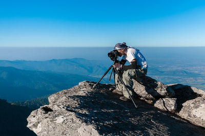 Man photographing on rock by sea against sky