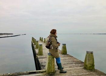 Side view of a woman resting against a mooring post of a wooden jetty in a mirror-smooth lake