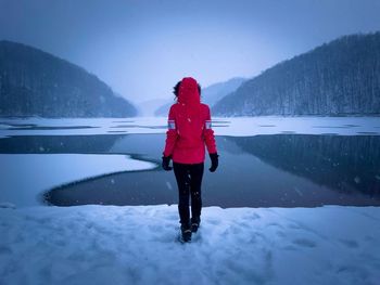 Rear view of woman with red coat standing in front of a frozen lake during winter