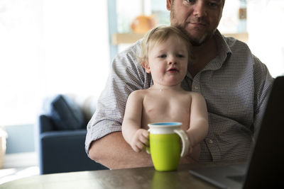 Dad working on computer, holding toddler boy drinking from sippy cup