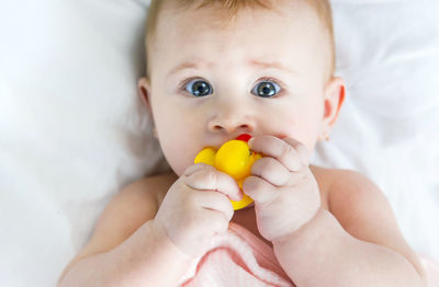 Close-up of cute baby girl holding toy lying on bed at home