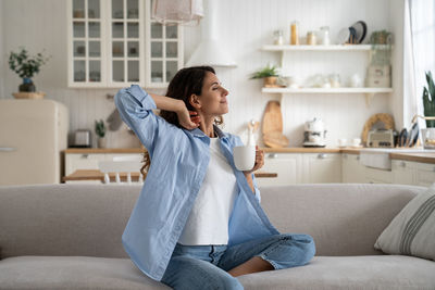 Portrait of young woman using phone while sitting on sofa at home