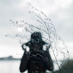 Defocused image of woman standing in front of plant against sky